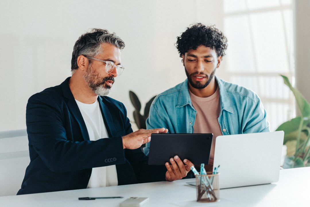 Two professional men collaborating in modern office using tablet and laptop