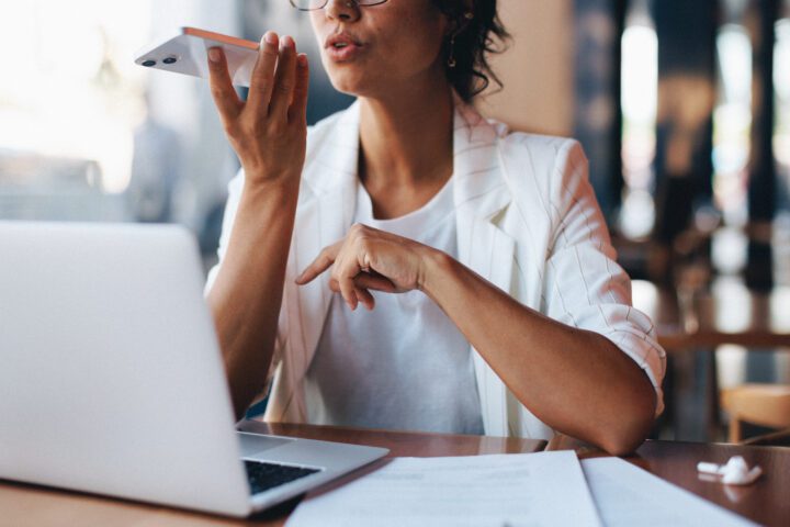 Businesswoman dictating a voice memo on smartphone while working at a cafe